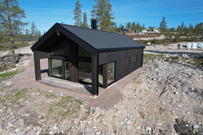 Skandināvu stila privātmāja ar dedzināta koka imitācijas fasādi, plašiem logiem un plašu apbūves laukum